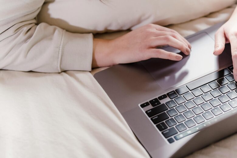 mujer tumbada en la cama con un ordenador portátil gris